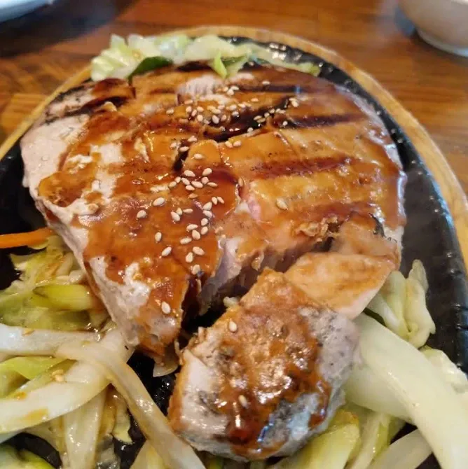 Placeholder photo: a grilled fish steak glazed with teriyaki sauce and sesame seeds on a sizzling plate